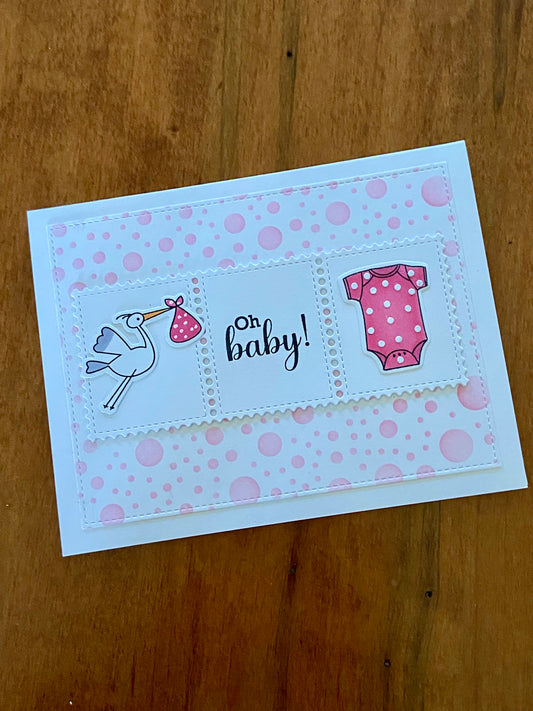 Oh Baby Shower card. Pink polka dot background. A rectangular centre panel with a stork carrying a pink bundle and pink onsie with tiny white dots and the sentiment Oh Baby in between. 