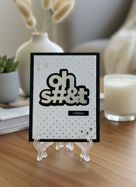 Funny belated birthday card with silver 'Oh Shit I Forgot' text and confetti on black cardstock with gold Swiss dot pattern displayed with birthday decorations