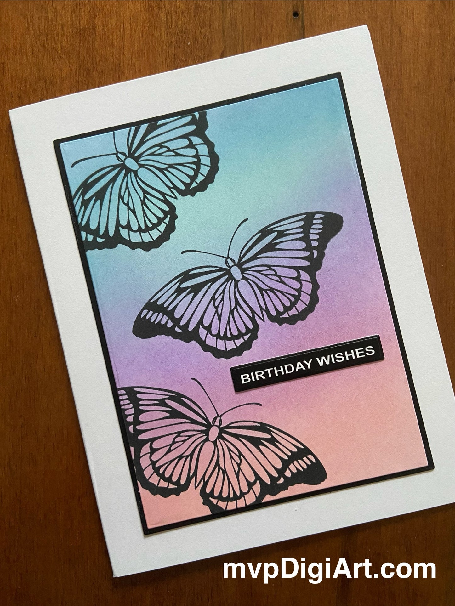 A handmade birthday card with a multicolored background featuring black silhouettes of butterflies and the text 'BIRTHDAY WISHES' on a panel with a white border.