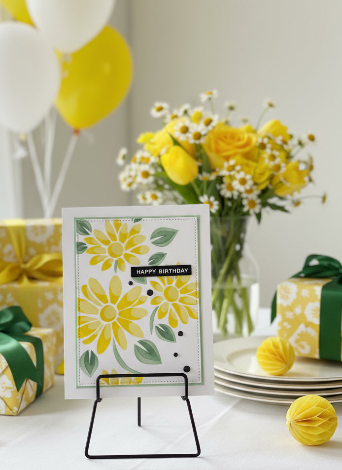 Yellow daisy birthday card with hand-stencilled design and black crystals displayed on a decorative stand with birthday decorations
