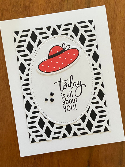 Handmade birthday card with a beach hat and a single stitched oval die cut, featuring black and white geometric pattern in the background, red hat, and black gems.