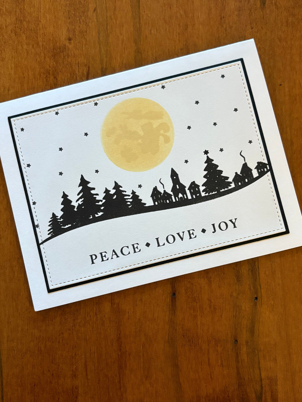 Greeting card with moon, trees, houses and 'Peace Love Joy' text 