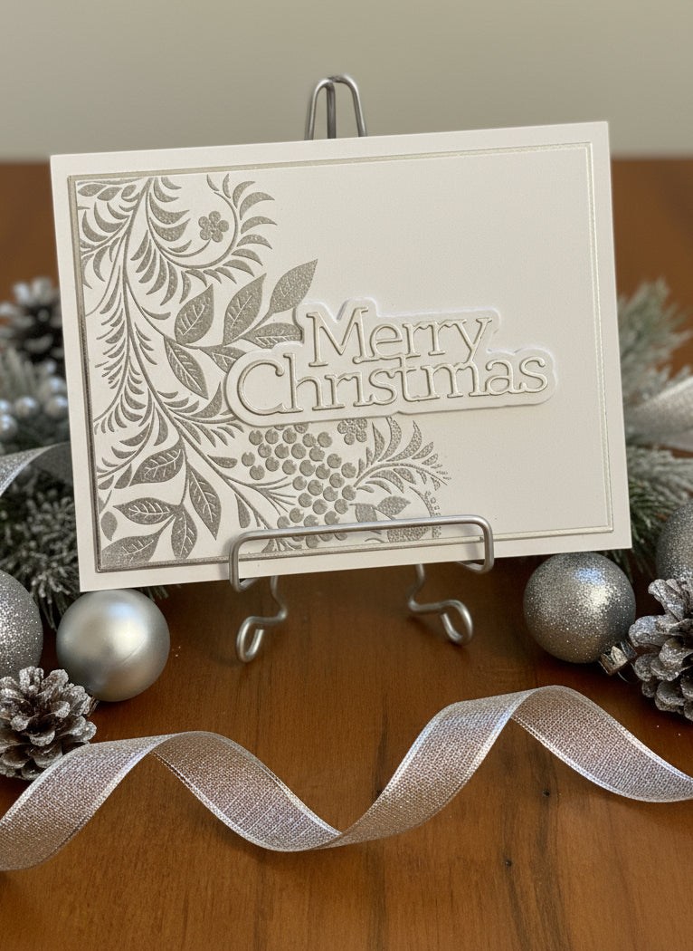Christmas card with silver and white embossed foliage displayed with festive holiday decorations