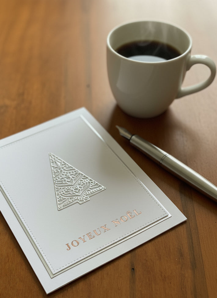 French Christmas card with silver filigree tree and Joyeux Noël greeting displayed on a desk with holiday decorations