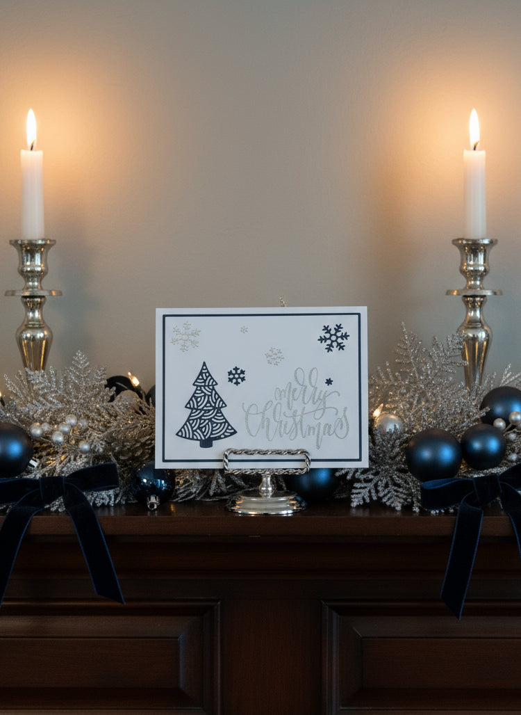 Christmas card with navy blue filigree tree and silver snowflakes displayed on a decorated mantle with holiday decorations