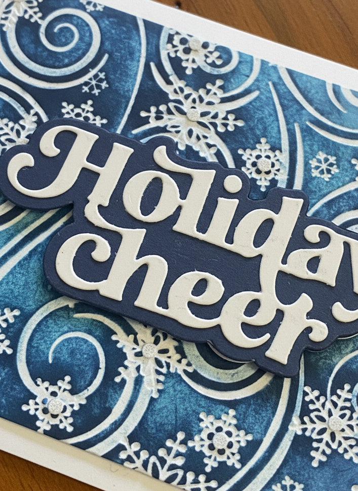Close-up detail of Christmas card showing blue and white swirling snowflakes with glitter accents and Holiday Cheer die-cut sentiment