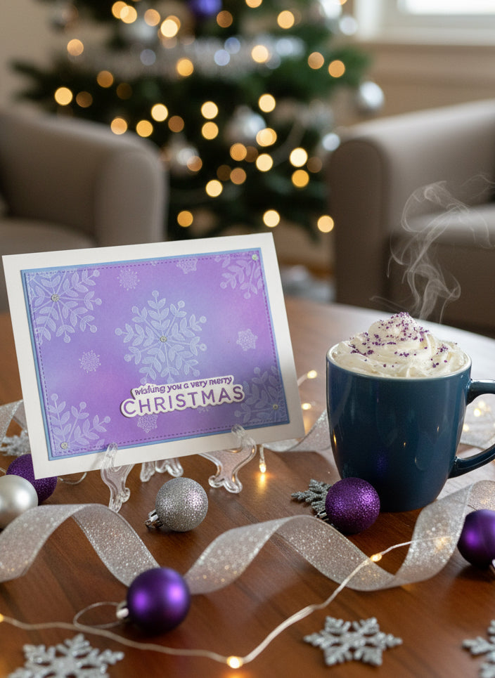 Handmade Christmas card with blue and purple ink blended background with a white snowflakes design with silver glitter accents displayed on a decorated table