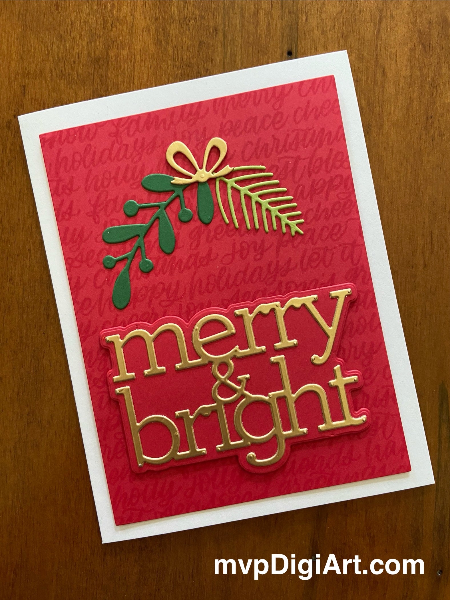 A handmade Christmas card with a red background featuring a die-cut sprig of spruce and a branch of leaves tied together with a lustrous gold bow, and the text 'merry & bright' in golden letters.