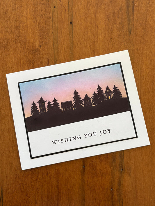 Greeting card with silhouette villiage and trees design against a sunrise and 'Wishing You Joy' text 