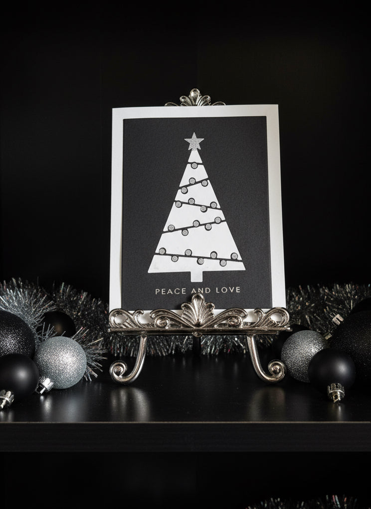 Modern geometric Christmas card with a tree design and 'Peace and Love' text, placed on a decorative stand with Christmas ornaments.