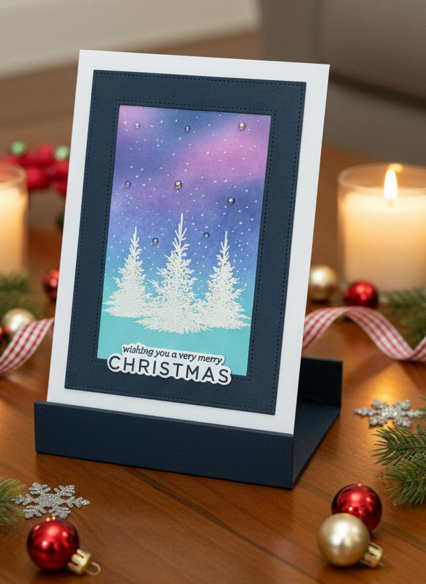 Handmade Christmas card with white spruce trees and snowy sky displayed on decorated surface