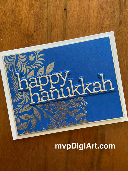 A handmade Hanukkah card with a blue background, silver vine with leaves and berry, the text 'happy hanukkah' in silver.