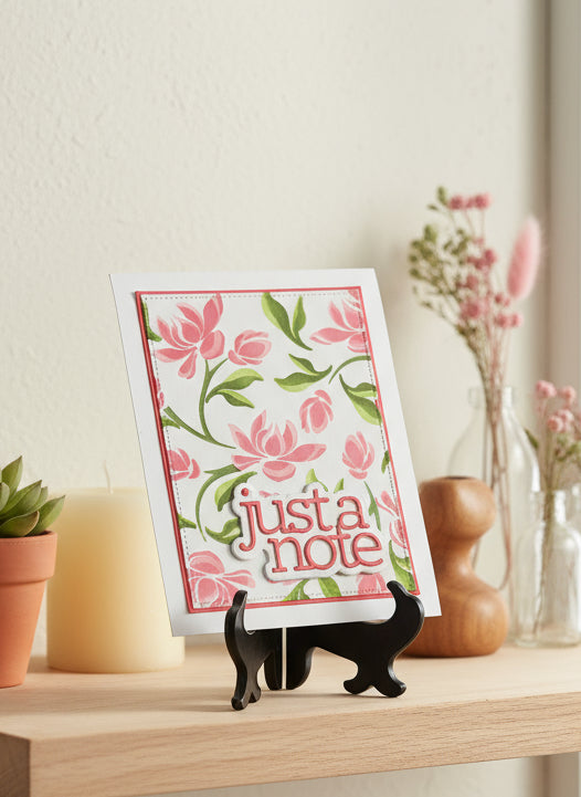 Pink floral and greeney card with 'just a note' text in a black stand on a decorated shelf