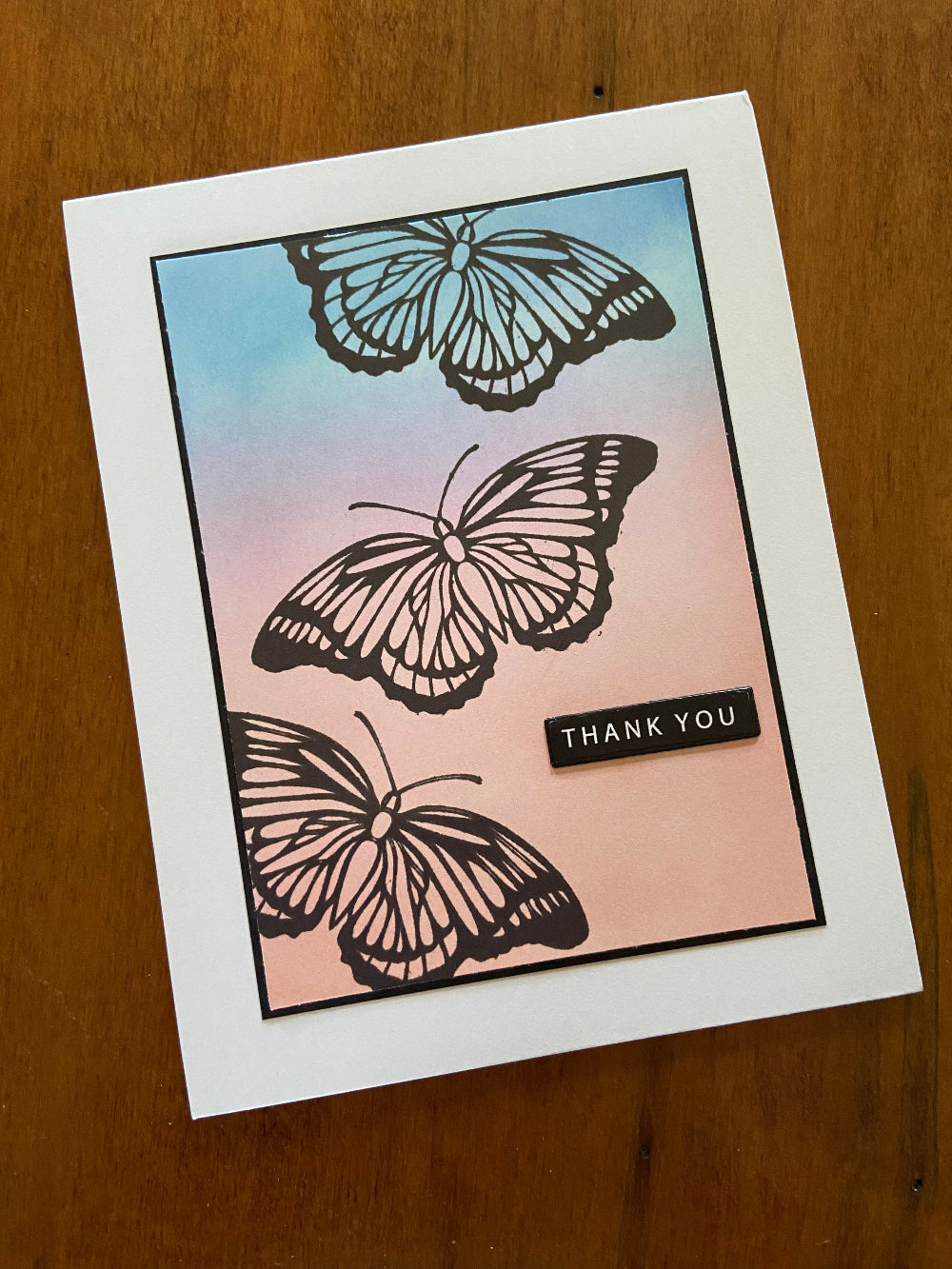 Silhouette Butterfly Thank You handmade card. Ink blended background in shades of peach, pink, purple and turquoise. 3 black butterflies are stamped across the card. A small black sentiment with white writing says 'thank you