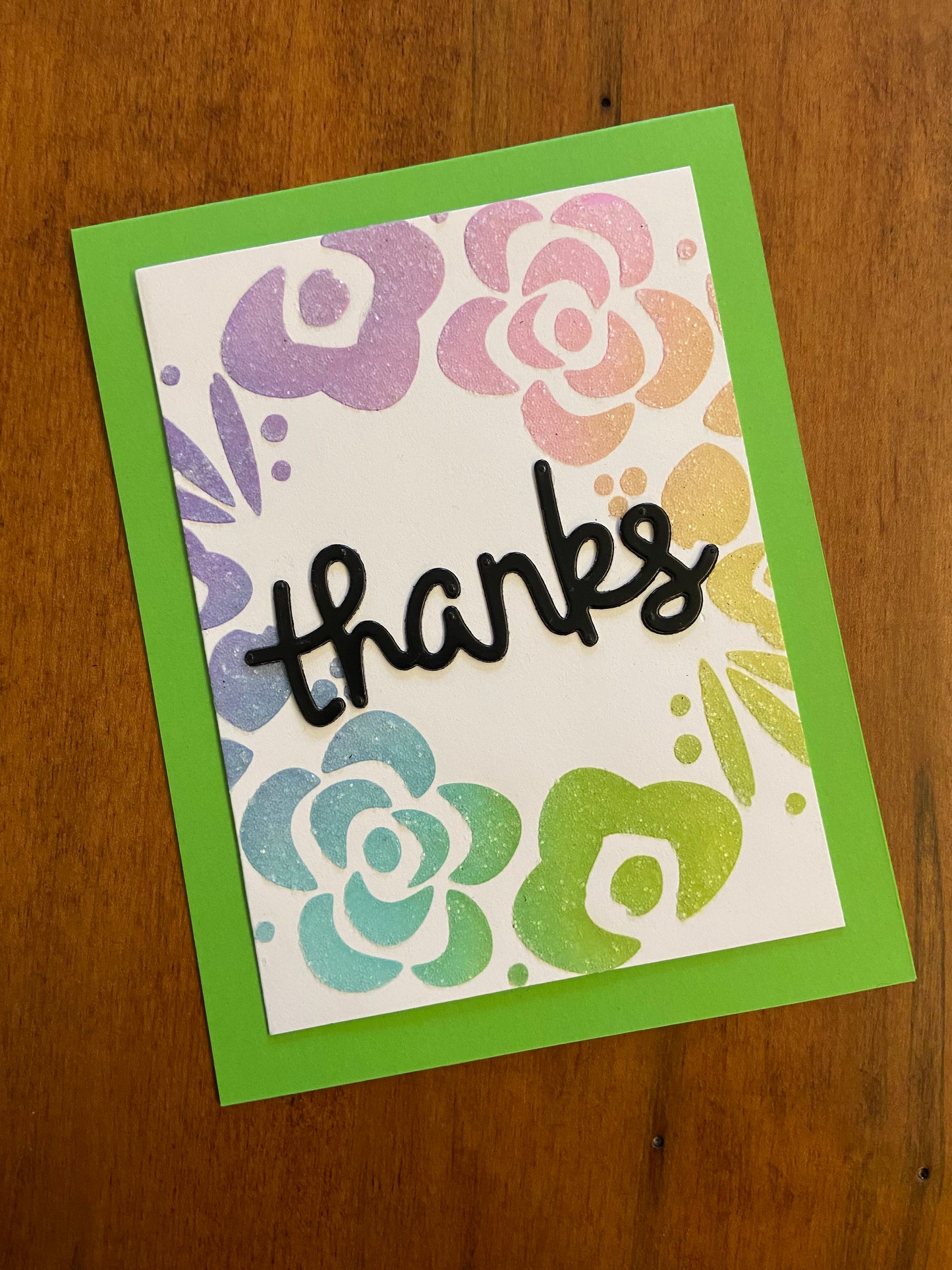 Handmade thank you card with pastel floral wreath in rainbow colours and glitter accents, black die cut 'thanks' in centre of wreath on green notecard