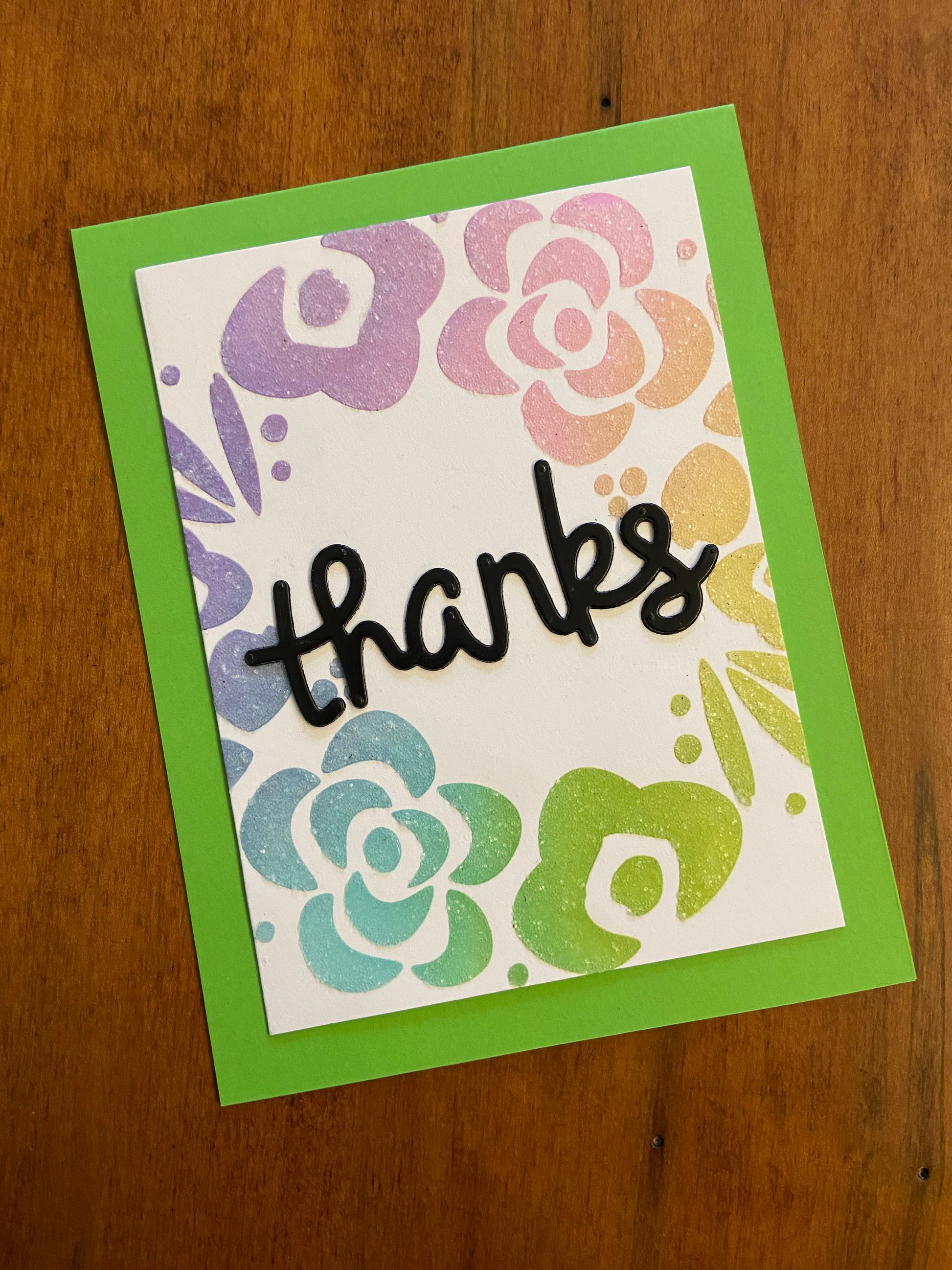 Handmade thank you card with pastel floral wreath in rainbow colours and glitter accents, black die cut 'thanks' in centre of wreath on green notecard