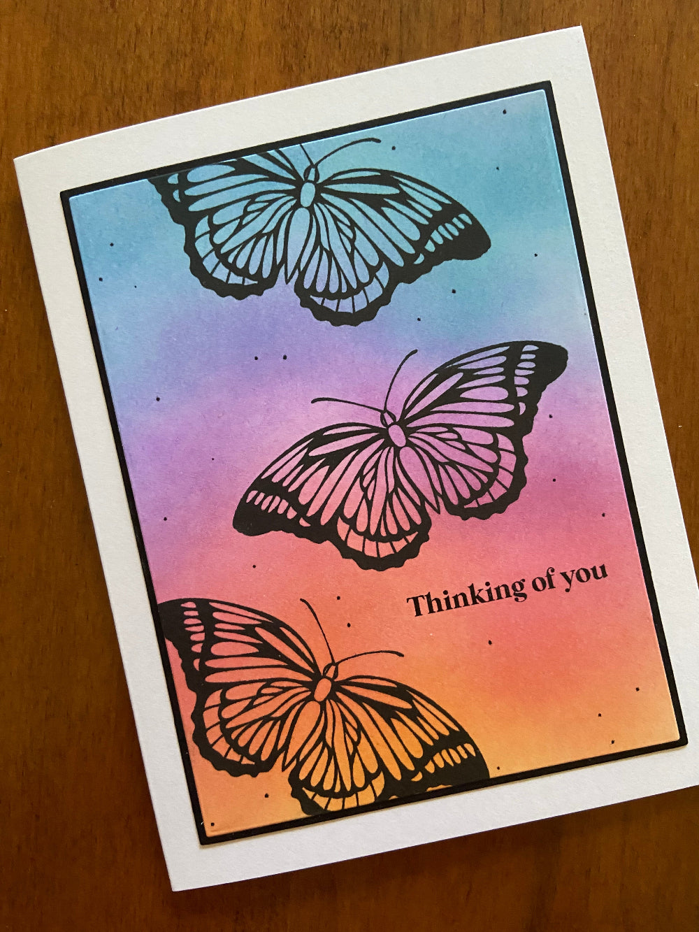 Silhouette Butterfly Thinking of You handmade card. Ink blended background in vibrant shades of orange, pink, purple and turquoise. 3 black butterflies are stamped across the card. 