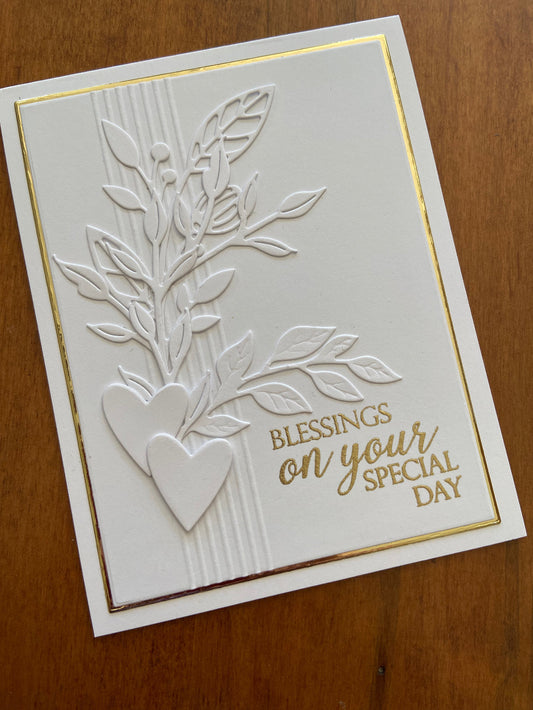 Handmade white-on-white wedding card with die-cut foliage bouquet and two modern hearts, gold heat-embossed "Blessings On Your Special Day" sentiment; panel layered on a shiny gold mat 