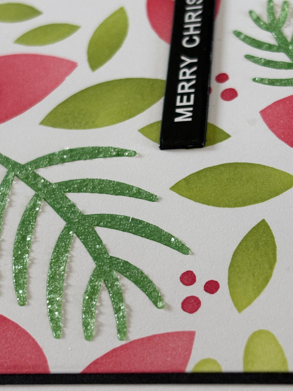 Closeup of a modern floral Christmas card featuring contemporary poinsettia design with red blooms and green foliage on white notecard; showing off sparkle texture. 