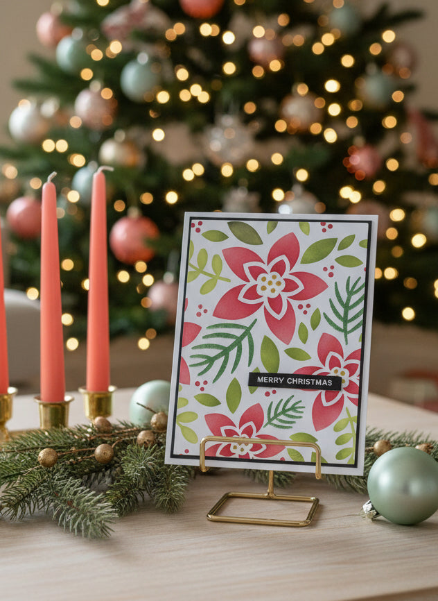 Christmas card with modern poinsettia floral design on a stand in front of a decorated Christmas tree.