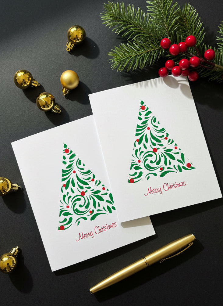 Two Christmas cards with tree designs on a dark surface with gold ornaments and greenery.