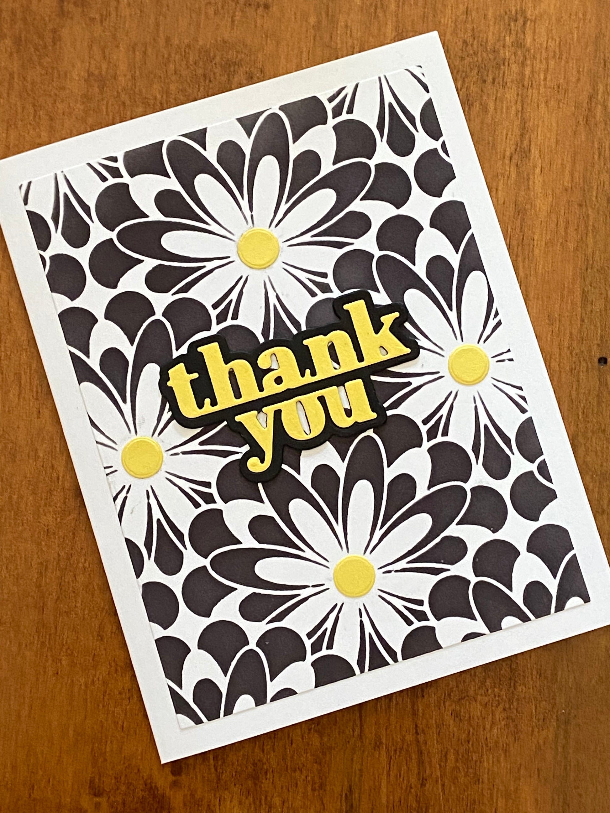 Black and white graphic daisies are ink blended onto the background.  Each daisy is completed with a bright  yellow centre.  To complete the card, a coordinating bold thank you die cut is adhered to the centre of the card.