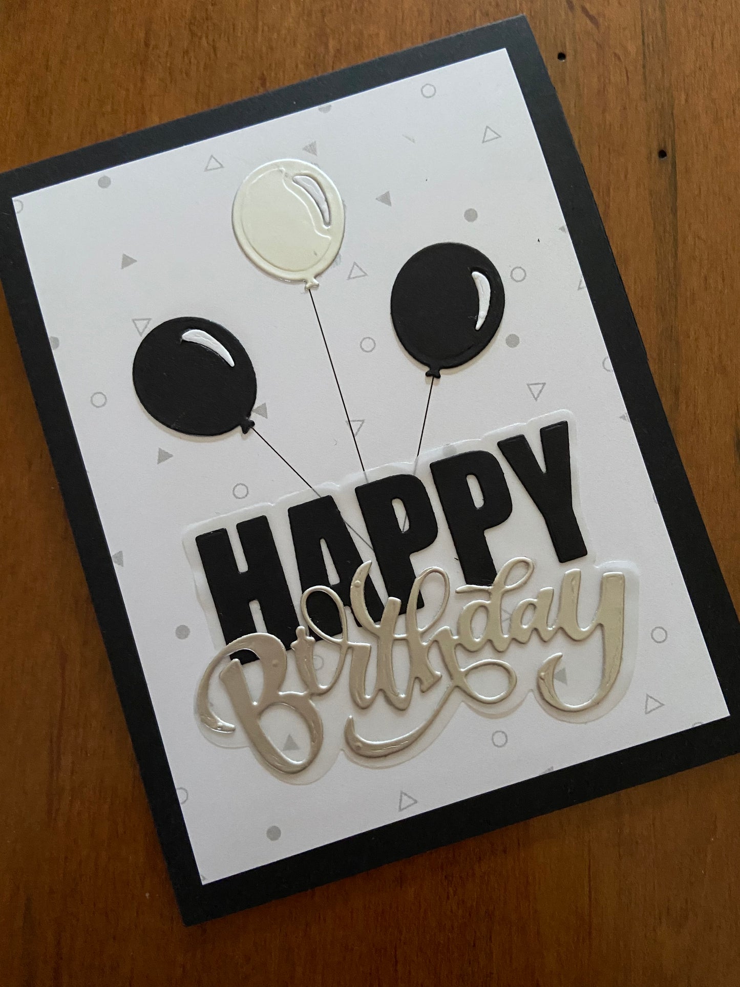 Black and silver balloons with a big black and sliver happy birthday die cut sentiment all mounted on a white panel with light grey confetti.