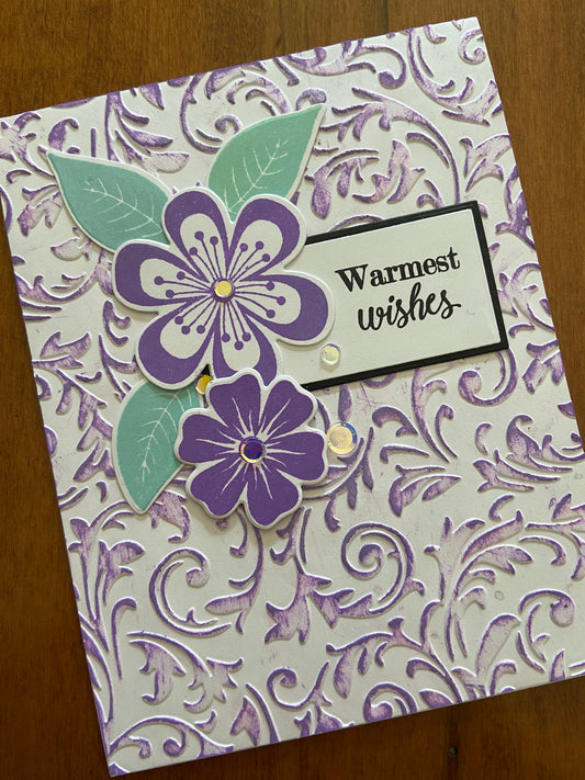 The embossed panel is lightly coloured with purple ink. This card is adorned with some purple flowers and leaf die cuts, a few silver embellishments for sparkle and a “warmest wishes” hand stamped sentiment is tucked in behind the flowers. 
