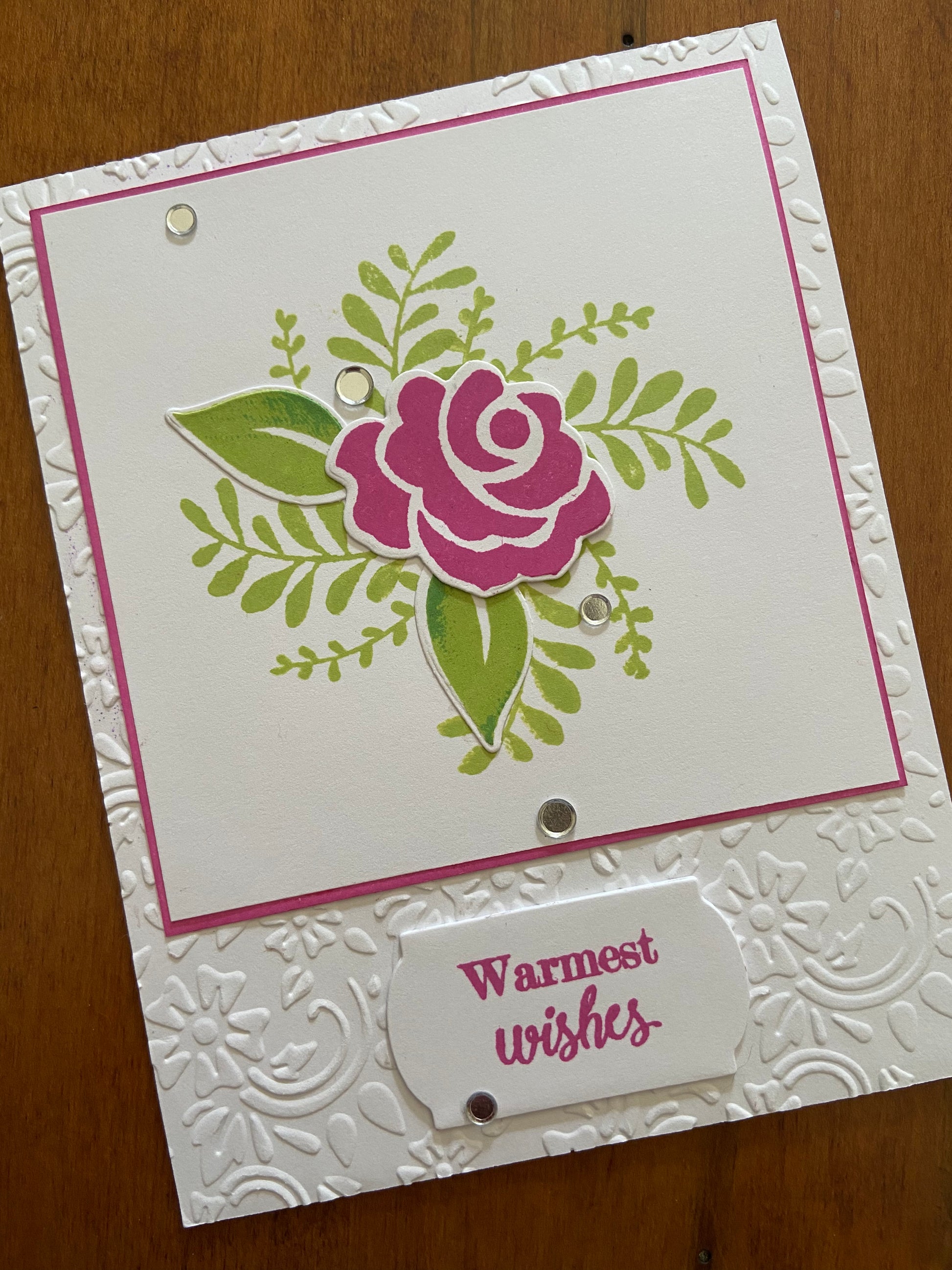 Warmest wishes handmade card. A graphic dark pink rose and greenery stamped and die cut on the front panel. 