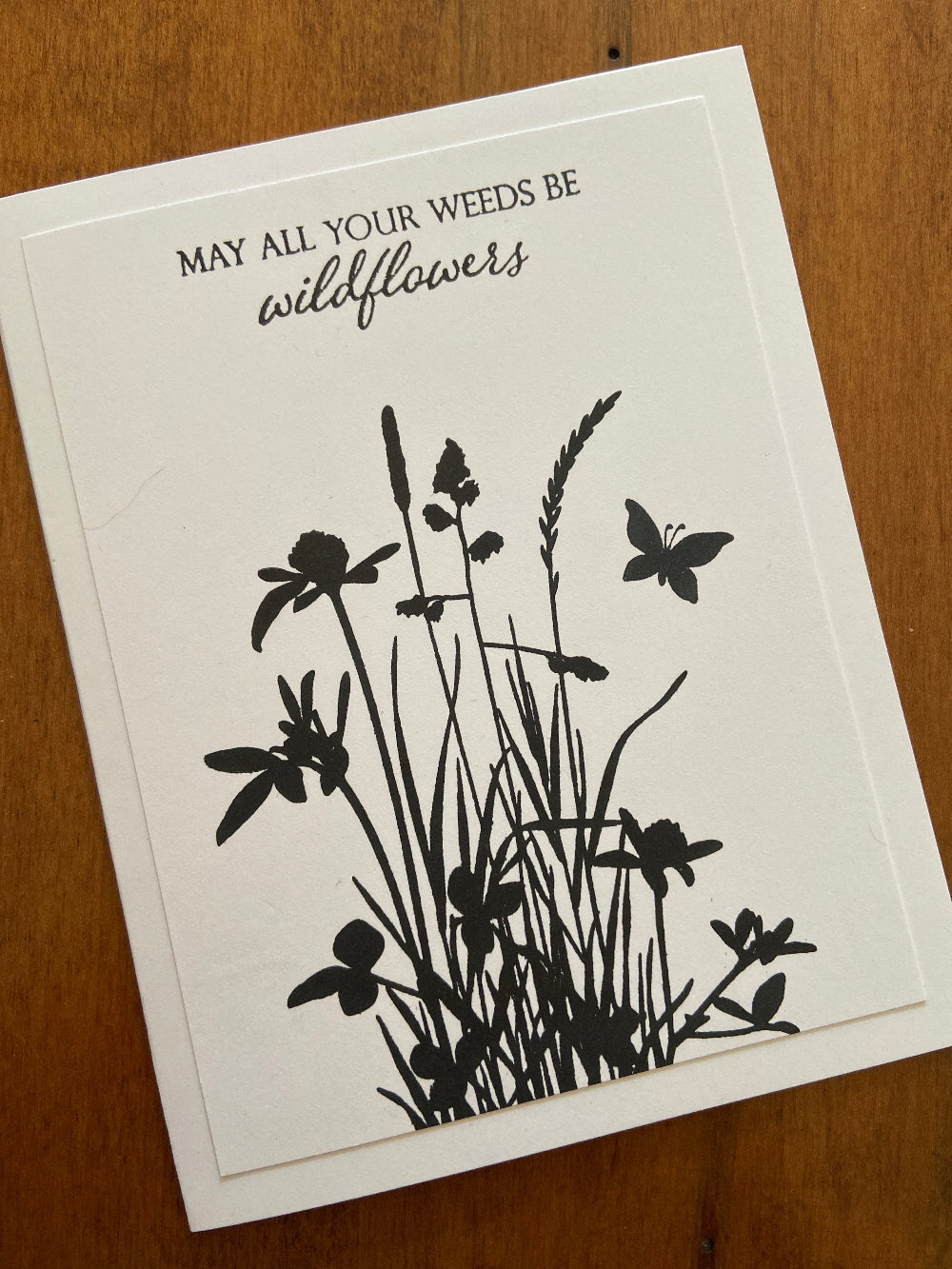 Handmade encouragement card with black wildflower silhouette and 'May all your weeds be wildflowers' sentiment on white background