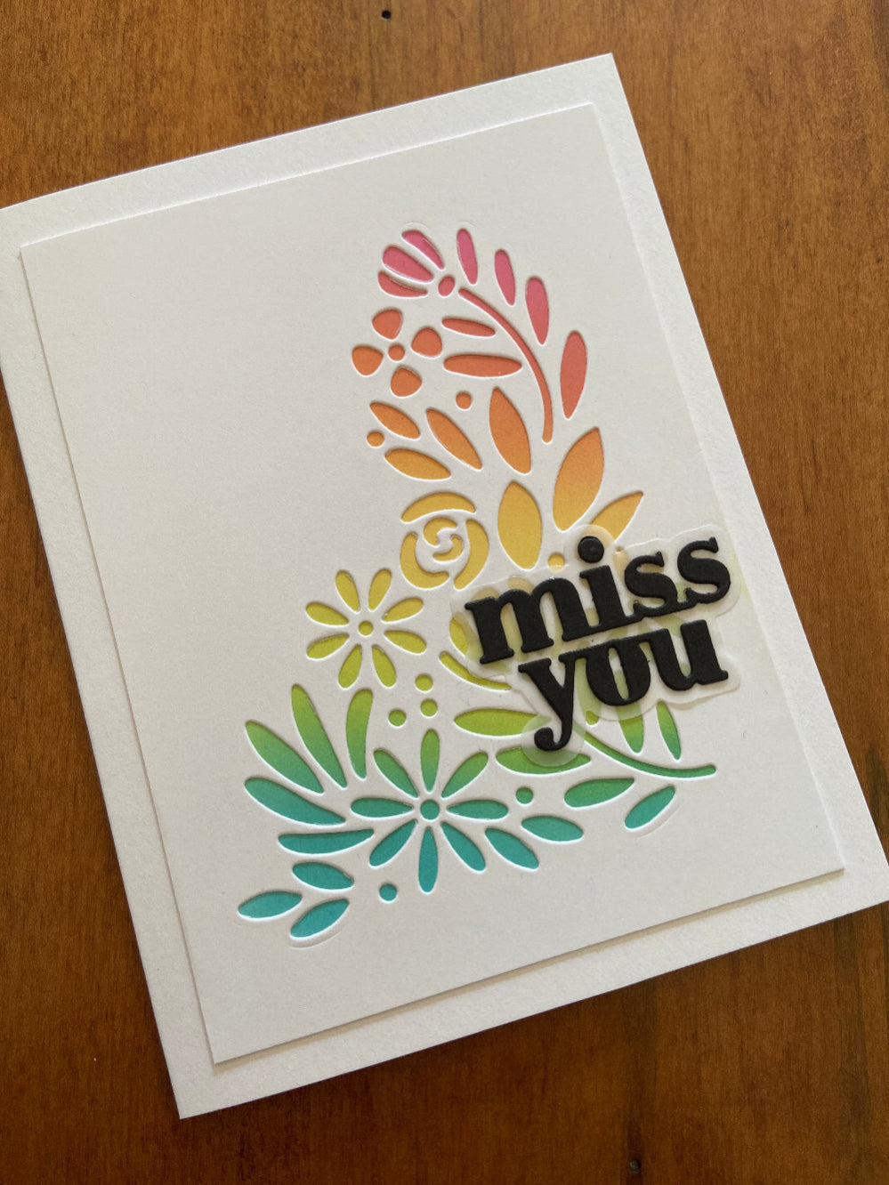 A handmade greeting card with 'Miss You' text and floral and foliage ink blended design with die cut overlay.