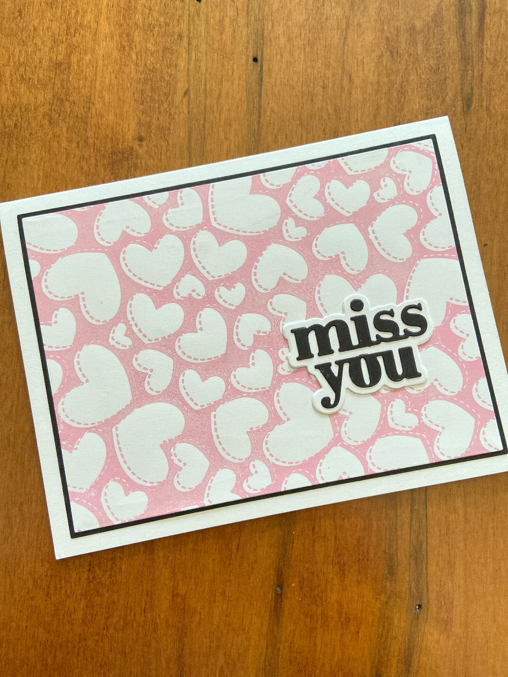 A handmade greeting card with a pink and white heart-stamped background, a black mat, and the words 'MISS YOU' in a die-cut shape on the front. 