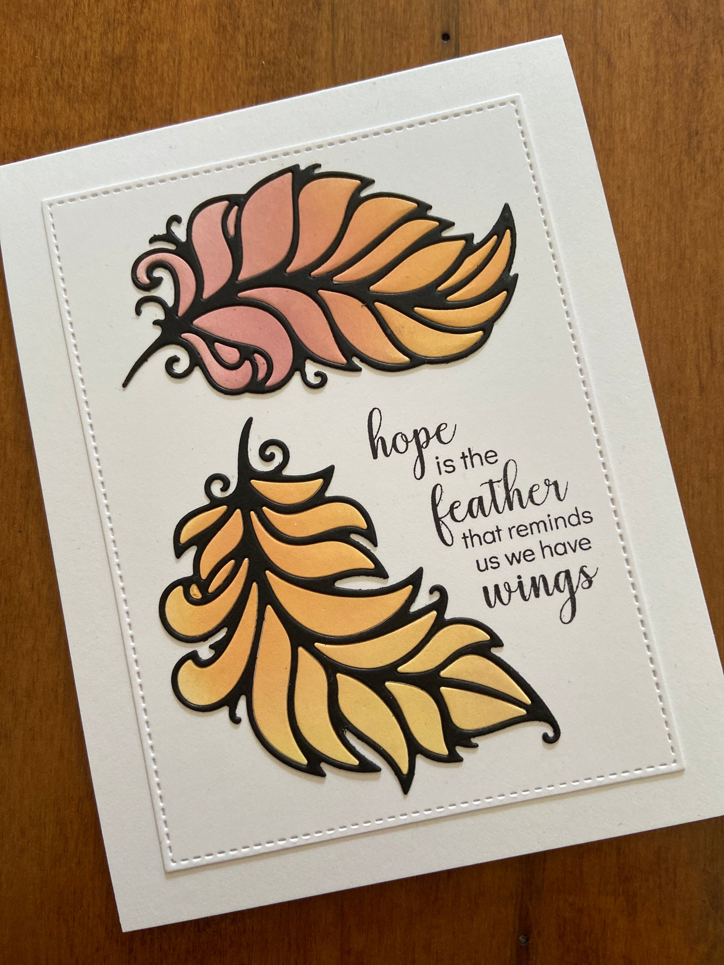 A white notecard with an encouraging hand stamped sentiment; 2 pink/orange ink blended feather die cuts adorn the card.